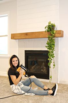 a woman sitting on the floor in front of a fireplace holding a blow dryer