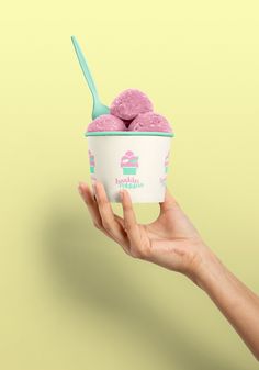 a hand holding an ice cream cup with pink toppings and a spoon in it