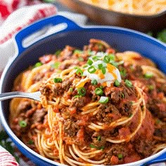 a blue bowl filled with spaghetti topped with meat, cheese and green onion garnish