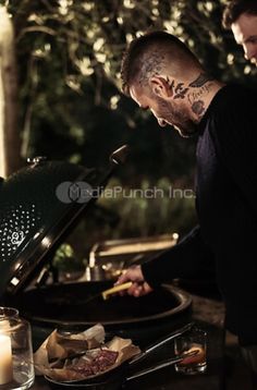 a man grilling food on an outdoor bbq with candles in front of him