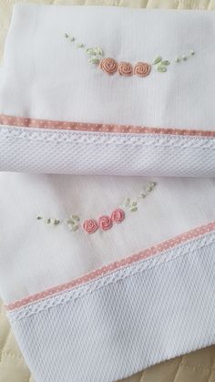 two pieces of white cloth with pink flowers and leaves embroidered on the edges, laying next to each other