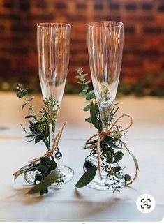 two champagne flutes with greenery in them are sitting on a table next to each other