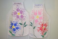 two aprons with hand prints on them are hanging up against the wall, and one has flowers painted on it