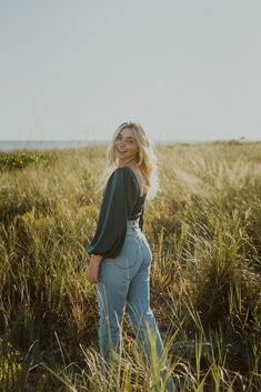 a woman standing in tall grass with her back to the camera and looking at the camera