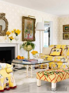 a living room filled with yellow furniture and flowers on the fireplace mantel, in front of a mirror