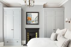 a white bed sitting in a bedroom under a chandelier next to a fireplace