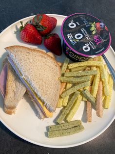 a sandwich, french fries and strawberries on a white plate with a container of ice cream