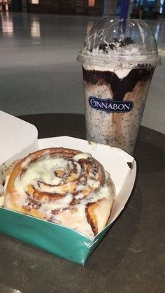 a cinnamon roll in a box next to a drink