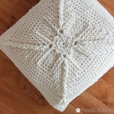 a white crocheted square sitting on top of a wooden floor next to a pillow