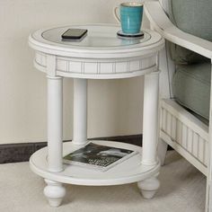 a small white table with a magazine on it next to a couch and coffee cup