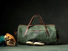 a green duffel bag sitting next to a pair of shoes and a blanket on the floor