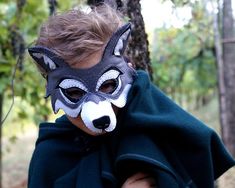 a young boy wearing a wolf mask and cape in front of a tree with leaves