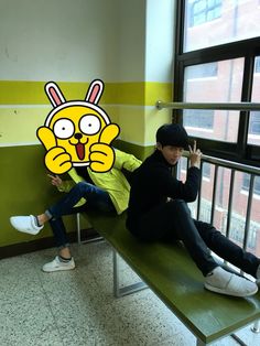 two people sitting on a bench in front of a wall with a cartoon character painted on it