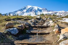 there is a trail going up the side of a mountain with rocks on it and snow capped mountains in the background