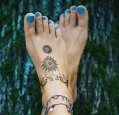 a woman's feet with tattoos and bracelets on her ankles next to a tree