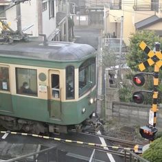 a green train traveling down tracks next to a traffic light and buildings in the background