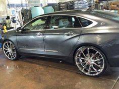 a grey car parked in a garage next to another car with chrome rims on it