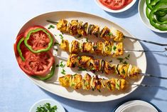 several skewers of food sit on a plate next to bowls of vegetables and sauces