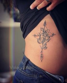 a woman's stomach with a cross tattoo on the side and flowers growing out of it