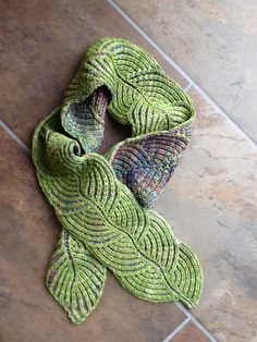 a green knitted scarf laying on top of a tile floor