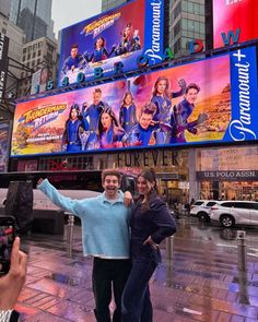 a man and woman standing in front of a billboard on the side of a building