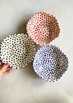 three polka dot bowls in different colors on a white surface with one hand reaching for the bowl