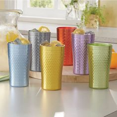 there are many different colored cups on the counter top with lemons and water in front of them