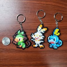 three keychains made out of pixelated video game characters on a wooden surface