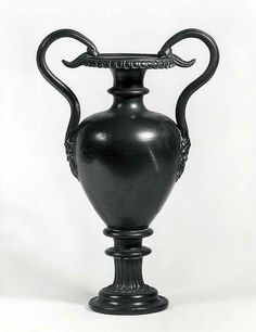 an ornate black vase with curved handles on a pedestal, against a white background or backdrop