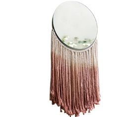 a round mirror with pink fringes hanging from it's sides and a circular mirror on the wall