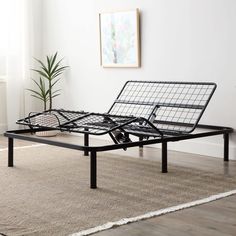 a metal bed frame sitting on top of a wooden floor next to a potted plant