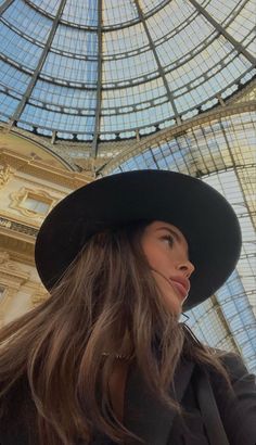 a woman with long hair wearing a black hat and looking up at the ceiling in a building