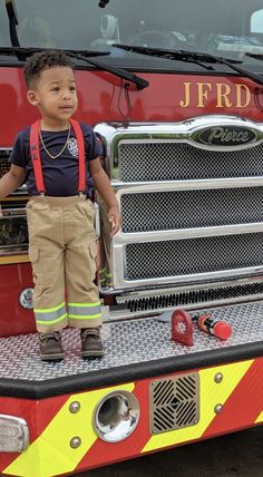 a young boy standing on the front of a fire truck with his hands in his pockets