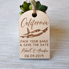 a wooden tag with an airplane and succulents attached to it that says, california pack your bags & save the date