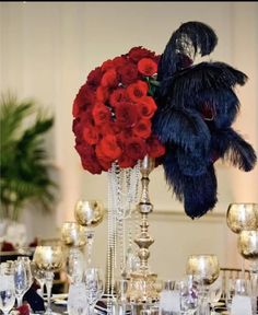 a vase filled with red roses and black feathers on top of a table covered in silverware