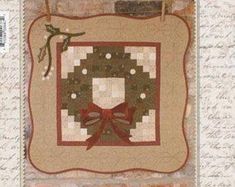 a quilted christmas wreath hanging on a brick wall with a red bow and ribbon