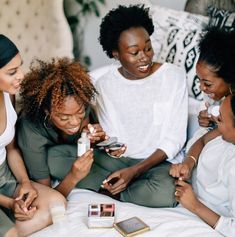 three women sitting on a couch looking at their cell phones and laughing while another woman holds her hand out