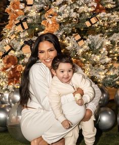 a woman holding a baby in front of a christmas tree