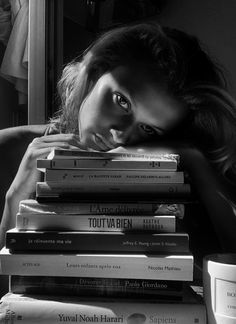 a woman leaning her head on top of a stack of books next to a cup