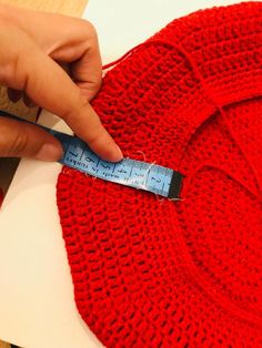 a person measuring the length of a red knitted sweater with a tape measure on it