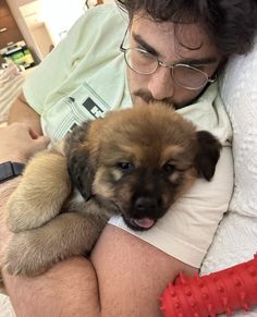 a man laying on top of a bed holding a brown and black puppy in his arms