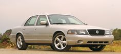 a silver car parked on the side of a road next to tall grass and trees