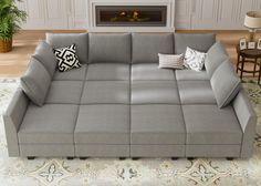 a gray couch sitting on top of a rug in front of a fire place with pillows