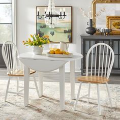 a white table with two chairs and a bowl of lemons on it in front of a chandelier