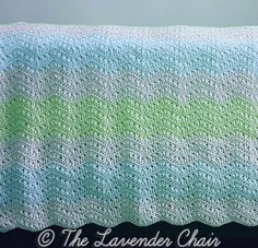 a crocheted blanket that has green and blue stripes on it, sitting on a table