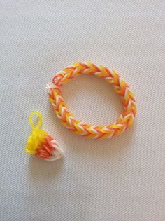 an orange, yellow and white braided bracelet next to a small plastic bead