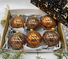 six shiny gold ornaments in a box on top of a table next to christmas decorations