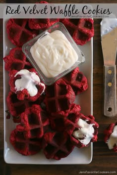 red velvet waffle cookies with white icing on a plate next to a knife and fork