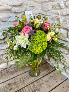 a vase filled with lots of flowers sitting on top of a wooden table next to a brick wall