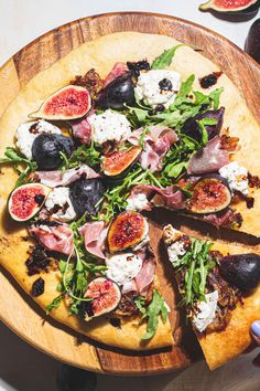 a pizza topped with figs and cheese on top of a wooden platter next to other foods